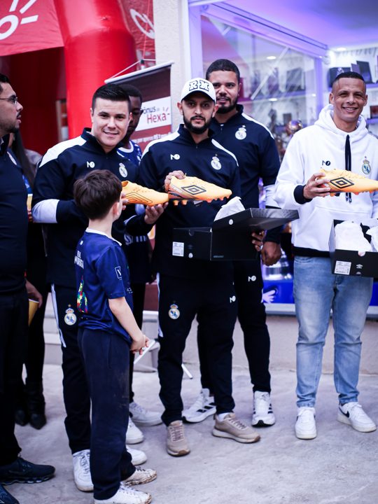Participantes posam com chuteiras douradas e embalagens Umbro; uma criança aparece em primeiro plano. Registro do Churrasco Fair Play, no acervo da SCP 2026.
