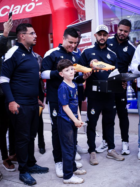 Grupo posa com os produtos Umbro em outro momento do encontro, com uma criança à frente. Registro do Churrasco Fair Play, no acervo da SCP 2026.