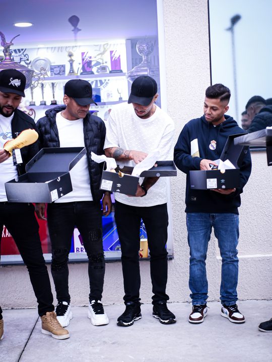 Quatro participantes manuseiam caixas e produtos Umbro. Registro do Churrasco Fair Play, no acervo da SCP 2026.