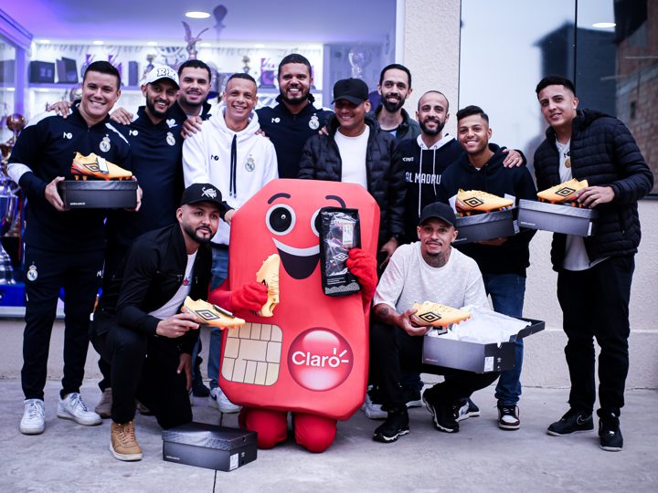 Participantes posam com chuteiras e caixas Umbro durante o Churrasco Fair Play. A mascote da Claro aparece no centro do grupo.