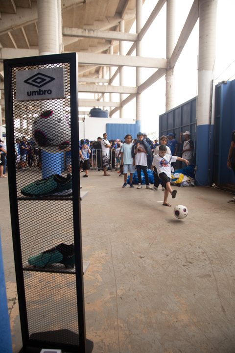 Expositor com a marca Umbro, bola e chuteiras em primeiro plano, enquanto o público participa de uma atividade com bola no espaço da Grande Final da SCP 2026.