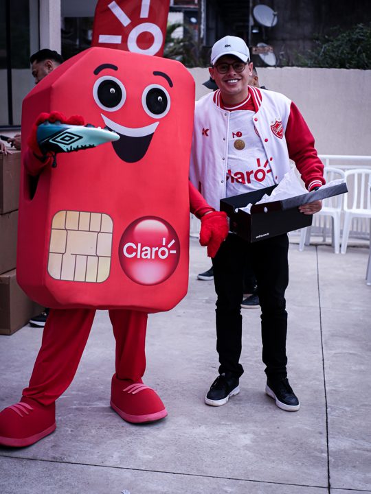 Participante segura uma caixa Umbro ao lado do mascote da Claro, que apresenta uma chuteira verde da marca. Registro do Churrasco Fair Play, no acervo da SCP 2026.