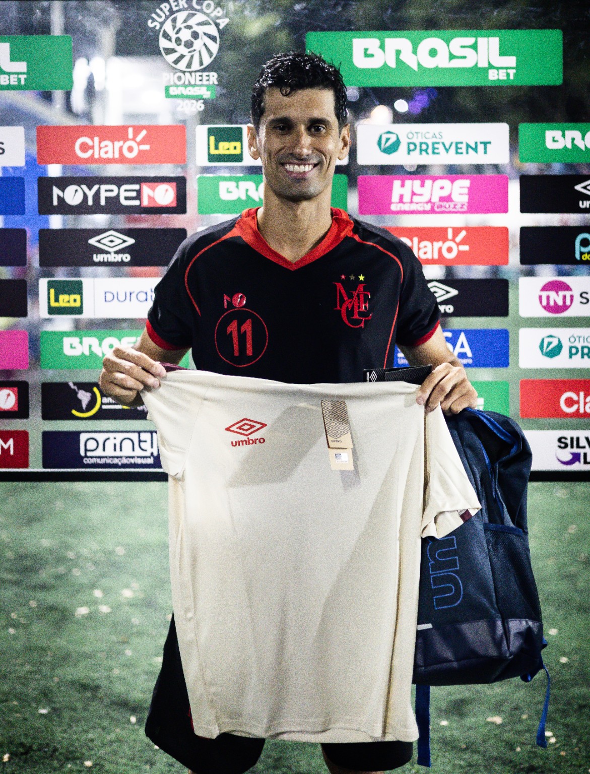 Atleta apresenta camiseta e bolsa Umbro diante do backdrop da SCP 2026, com a marca também aplicada no painel. O original 787A3180.jpg foi localizado na pasta Abertura / Iagueira. Identificação do atleta e critério da premiação a confirmar.
