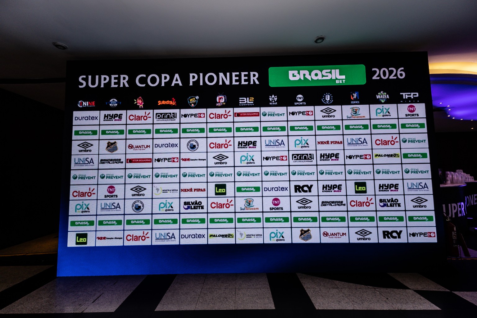 Painel da Super Copa Pioneer 2026 com o logotipo Umbro entre os patrocinadores. O original 787A0720.jpg integra a pasta Congresso / Iago do acervo da competição.
