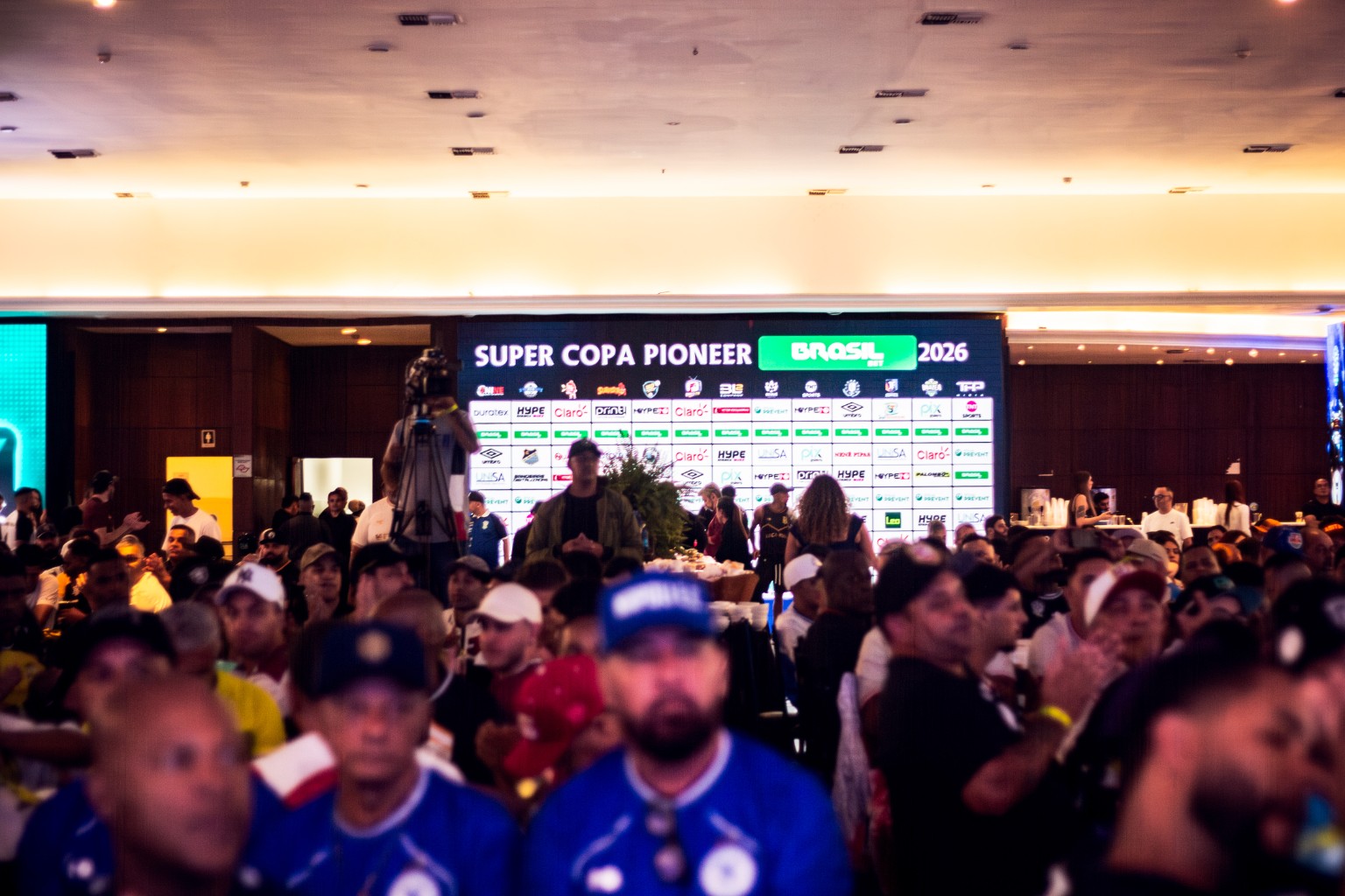 Vista do Congresso Técnico da SCP 2026, com público e painel de patrocinadores ao fundo, incluindo a Umbro. O original IMG_0492.jpg foi localizado na pasta Congresso / Ronan.