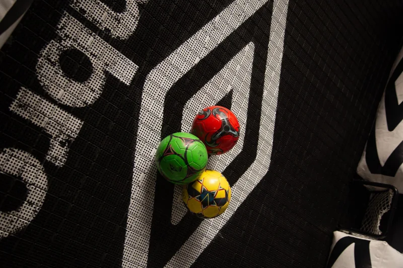Vista em ângulo de três bolas coloridas sobre o piso personalizado com o nome Umbro e o duplo diamante.