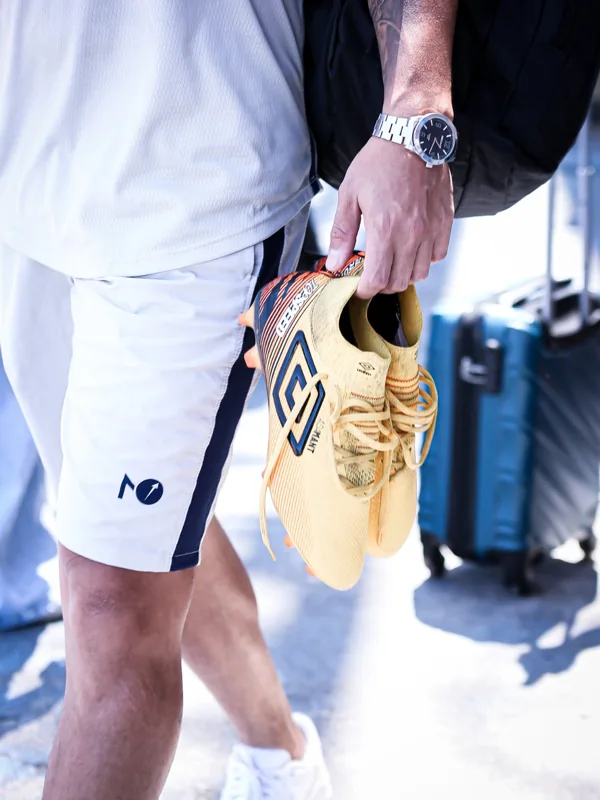 Pessoa com roupa esportiva branca segura um par de chuteiras douradas, com o duplo diamante Umbro visível nas laterais.
