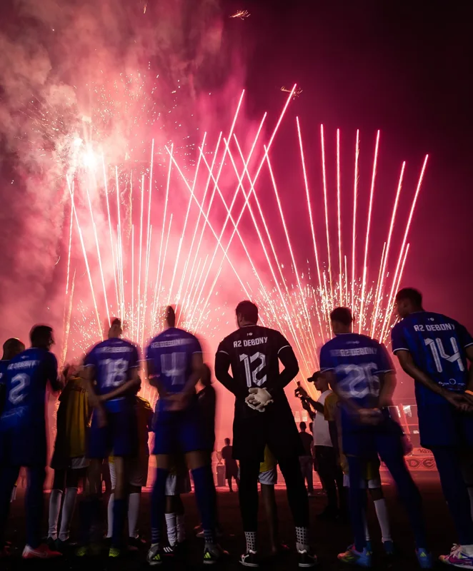 Outro enquadramento dos jogadores de azul e dos fogos no ambiente da Super Copa Pioneer. Registro de contexto geral da competição.