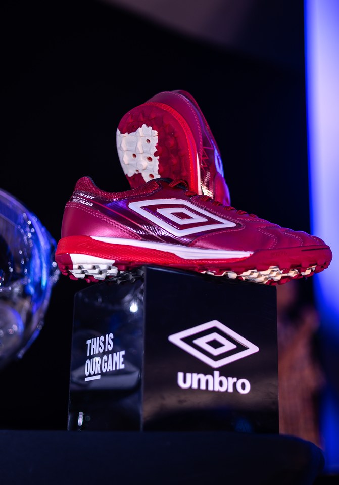 Chuteiras magenta Umbro sobre um expositor com o duplo diamante e a assinatura “This is our game”, no Congresso Técnico da SCP 2026.