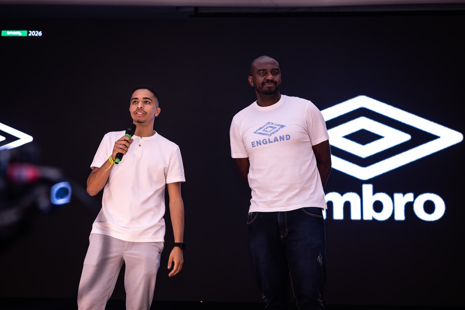Dois participantes no palco, um deles ao microfone, diante da marca Umbro em destaque no painel do Congresso Técnico da SCP 2026. O registro não mede a duração da exposição ou o conteúdo das falas.