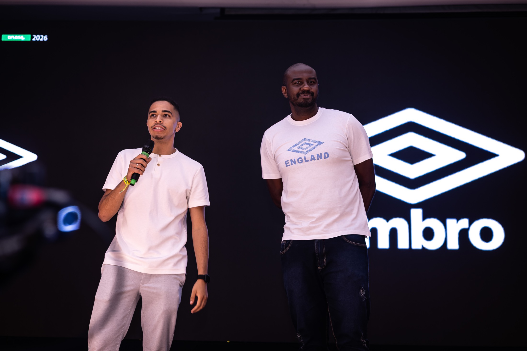 Dois participantes no palco, um deles ao microfone, diante da marca Umbro em destaque no painel do Congresso Técnico da SCP 2026. O registro não mede a duração da exposição ou o conteúdo das falas.