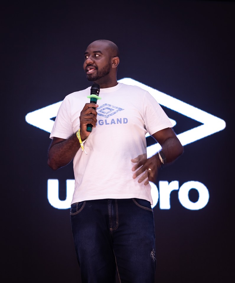 Participante fala ao microfone usando camiseta com o duplo diamante Umbro, diante do painel que também exibe a marca no Congresso Técnico. Identificação e função do participante a complementar.