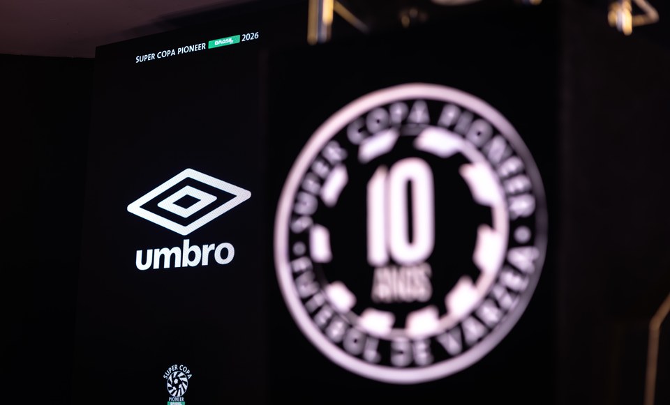Logotipo Umbro em foco no painel do Congresso Técnico, ao lado do símbolo dos 10 anos da SCP em primeiro plano desfocado. Registro da comunicação visual de 2026.