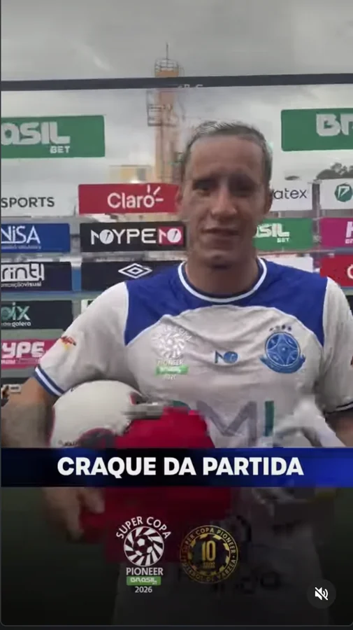 Participante de uniforme branco e azul aparece com uma bola e uma peça de vestuário durante o conteúdo “Craque da partida”. A marca Umbro está visível no painel ao fundo. Registro enviado pela Scout Sports para o acervo do Hat-trick Umbro.