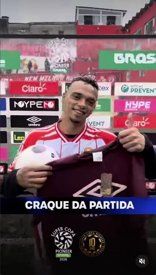 Participante apresenta uma camiseta com o duplo diamante Umbro e segura uma bola, diante do painel de patrocinadores. A captura exibe a identificação “Craque da partida”. Registro enviado pela Scout Sports para o acervo do Hat-trick Umbro.