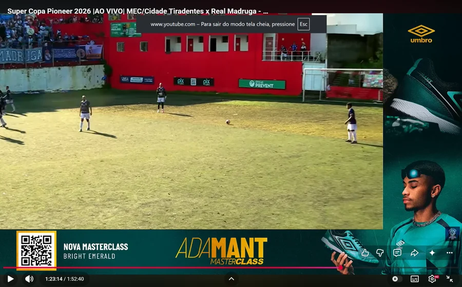 Banner Umbro em L durante MEC/Cidade Tiradentes × Real Madruga: faixa lateral e inferior com produtos, atleta da campanha, QR code e “Adamant Masterclass · Bright Emerald”. O player marca 1:23:14.