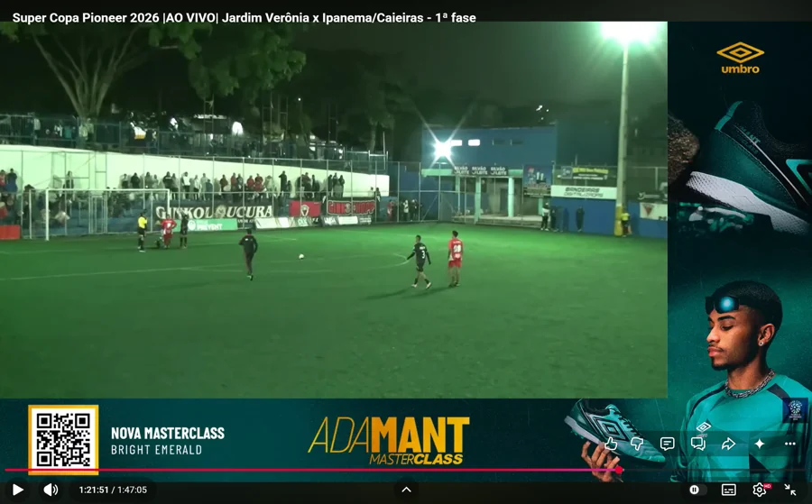 Banner Umbro em L durante Jardim Verônia × Ipanema/Caieiras, com produto, QR code e a campanha “Adamant Masterclass · Bright Emerald”. O título identifica a primeira fase e o player marca 1:21:51.