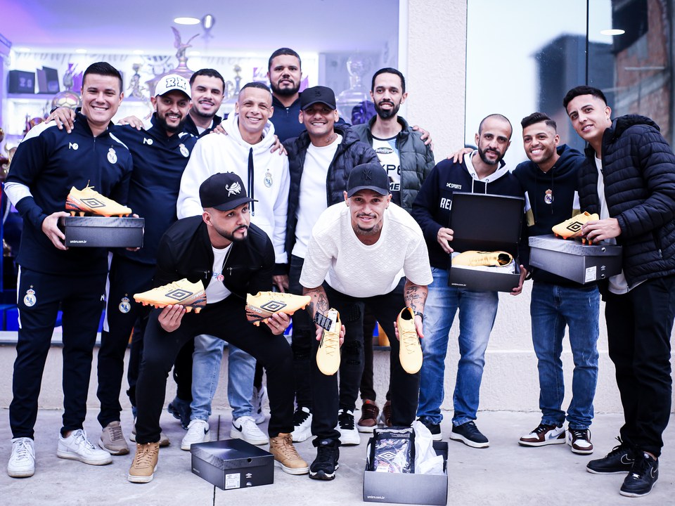 Participantes exibem chuteiras amarelas e caixas Umbro no encontro registrado no acervo “Churrasco Claro + Chuteira Umbro” da SCP 2026. A fotografia registra os produtos com o grupo; nomes, critérios e total de contemplados a confirmar.