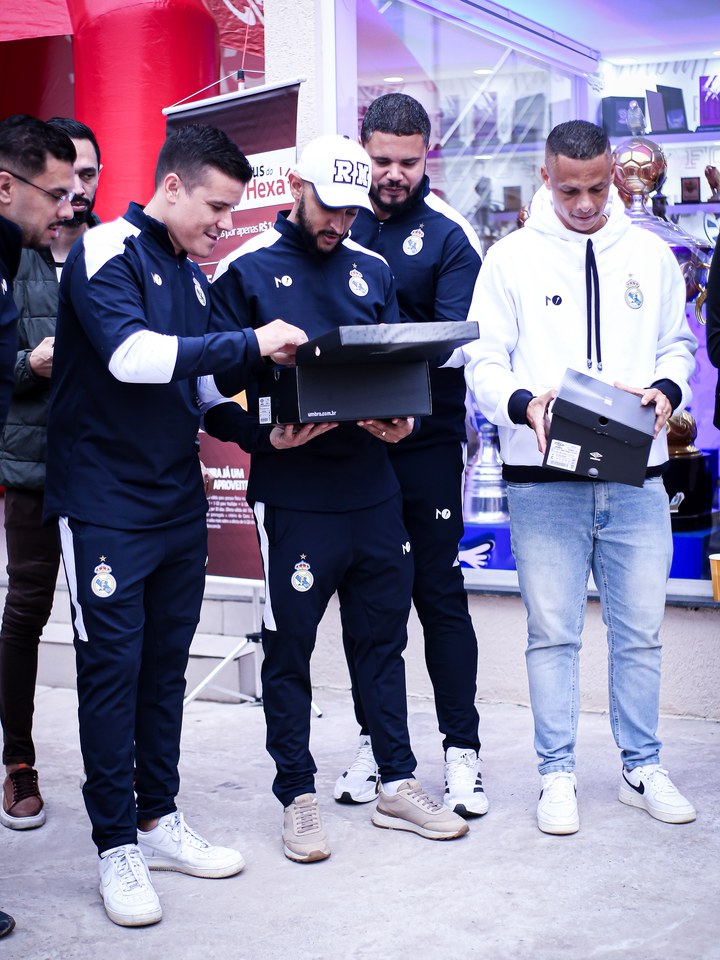 Participantes abrem e apresentam caixas identificadas com a marca Umbro. Registro localizado no acervo do encontro “Churrasco Claro + Chuteira Umbro”, na SCP 2026. Identificação nominal e quantidades totais a confirmar.